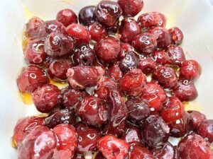 There are cherries in a white casserole dish with corn syrup on top.