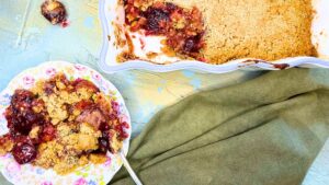 There is a cherry crumble with a scoop out of it. There is a floral plate with a serving of cherry crumble.