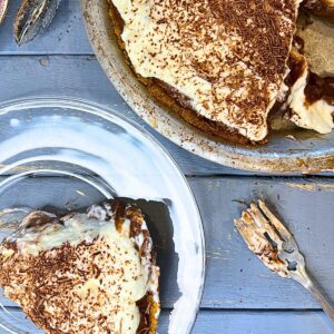 A chocolate pie with a whipped cream topping with a slice out of it. There is a slice of the pie on a glass plate in front.