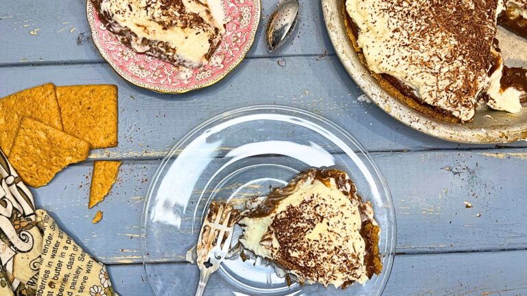 A chocolate cream pie with a slice out of it. There is a slice of pie in the front on a glass plate and another slice in the background on a pink plate.