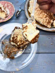 There is a woman holding a forkful of chocolate cream pie. The rest of the pie is in the background.