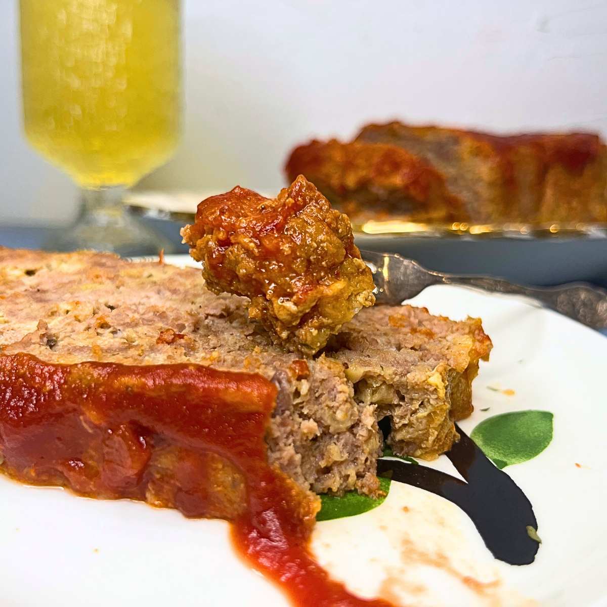 There is a slice of meatloaf of a plate with a fork full resting on top.