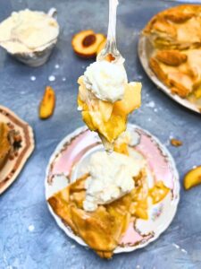 There is a woman holding a fork full of peaches with cream on it. There is a pie in the packground.