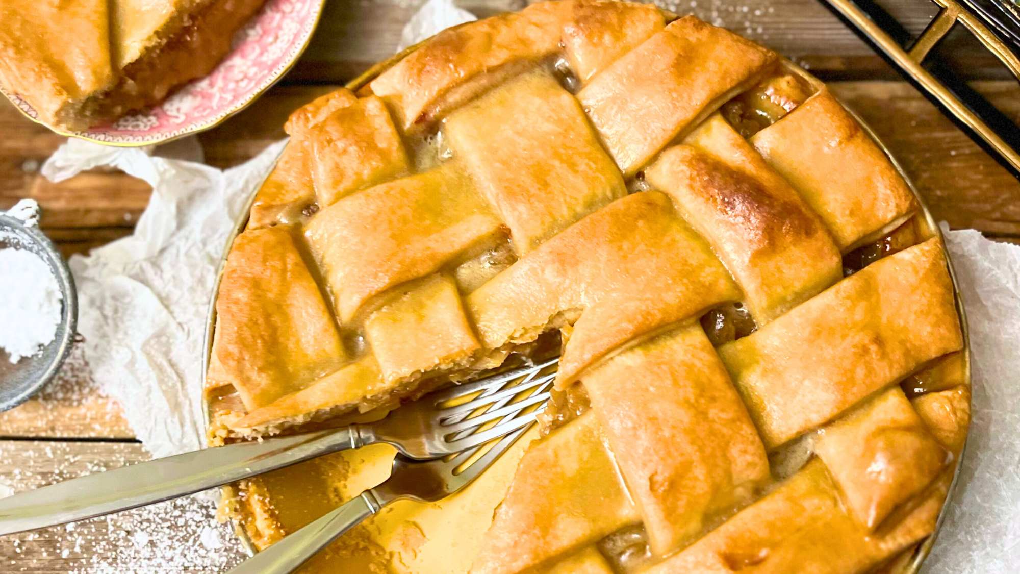 There is a wide lattice top pie on a wooden table. There is a slice out of it.