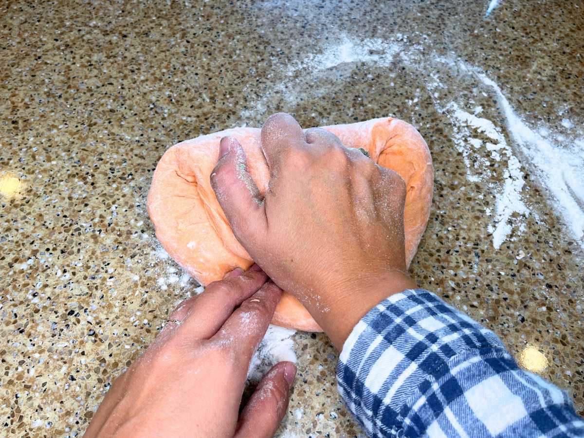 A woman kneading orange dough.