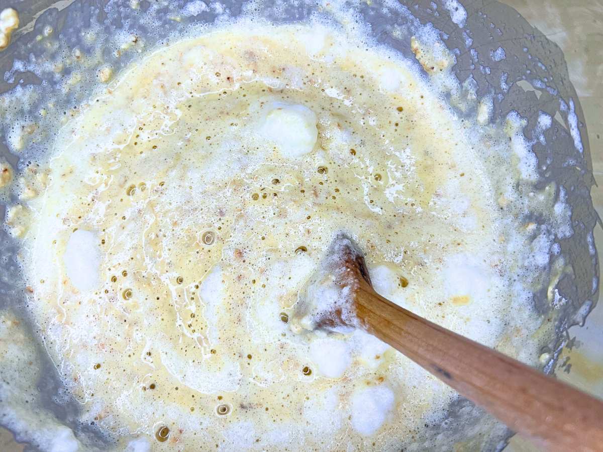 There is oatmeal pancake batter in a metal bowl with a wooden spoon.