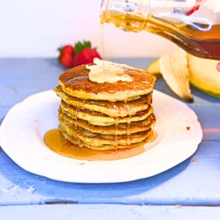 There is a woman pouring maple syrup onto a stack of pancakes.