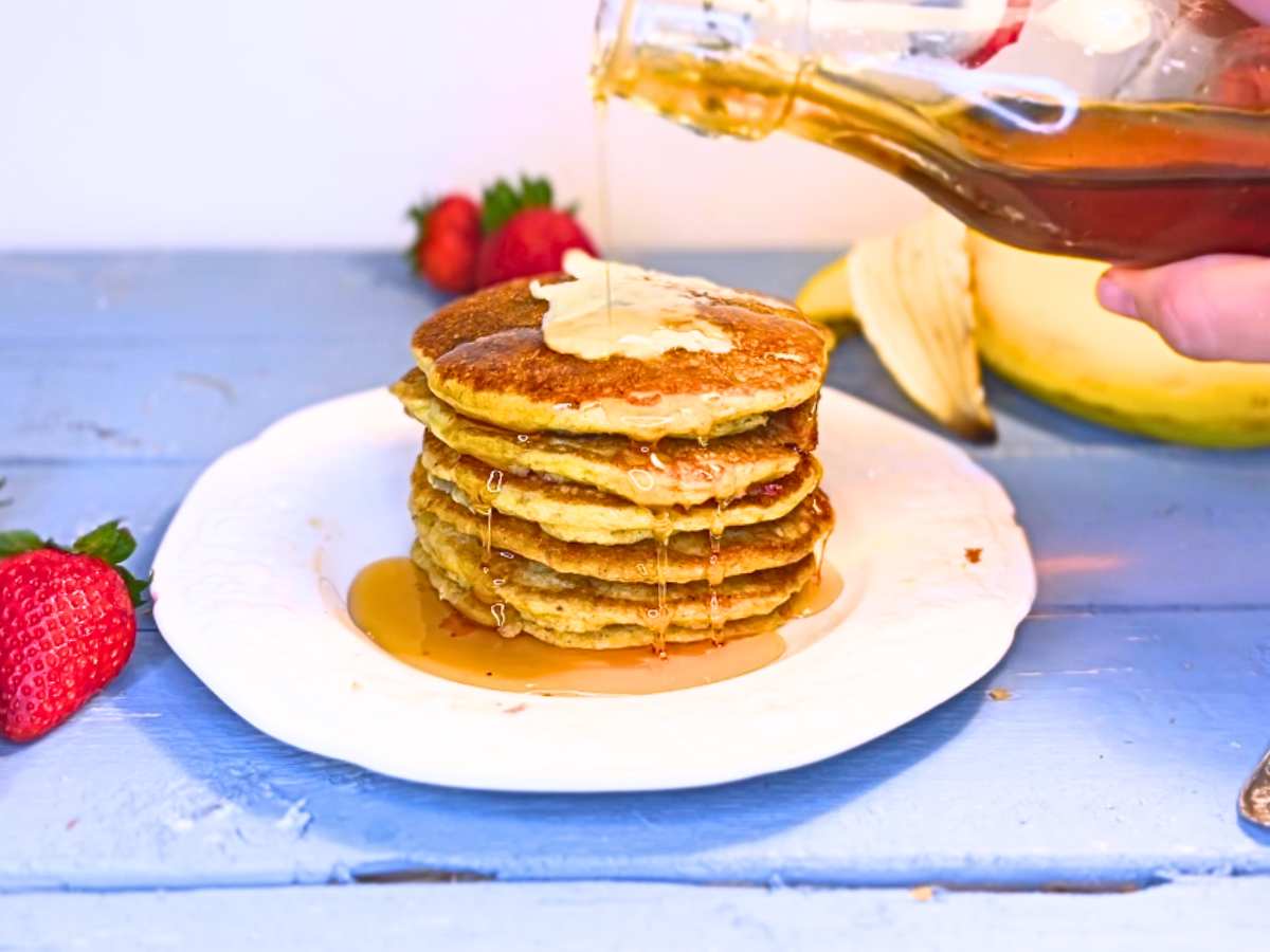 There is a woman pouring maple syrup onto a stack of pancakes.