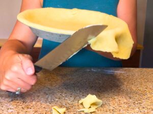 There is a woman trimming pie dough with a knife.