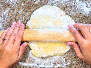 A woman rolling out dough with a wooden rolling pin.