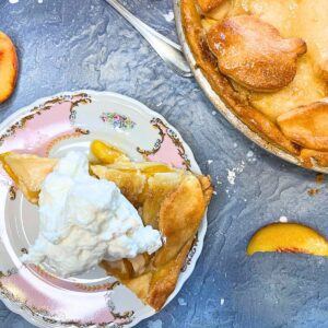 There is an overhead look at a slice of peach pie on a a pink floral plate. There is more of the pie off to the side.