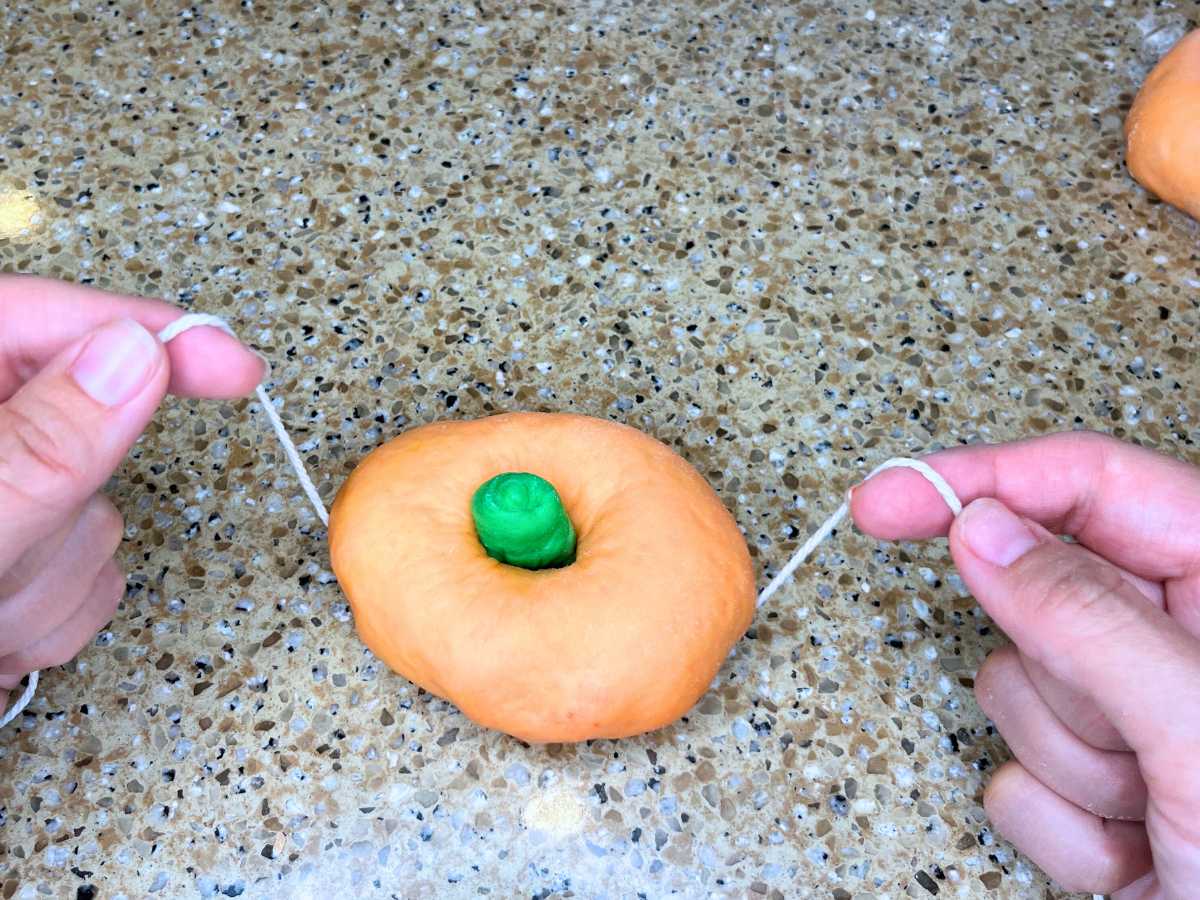 A woman holding a piece of kitchen twine under orange and green dough.