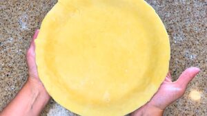 A woman is holding a lined pie plate with pie dough.