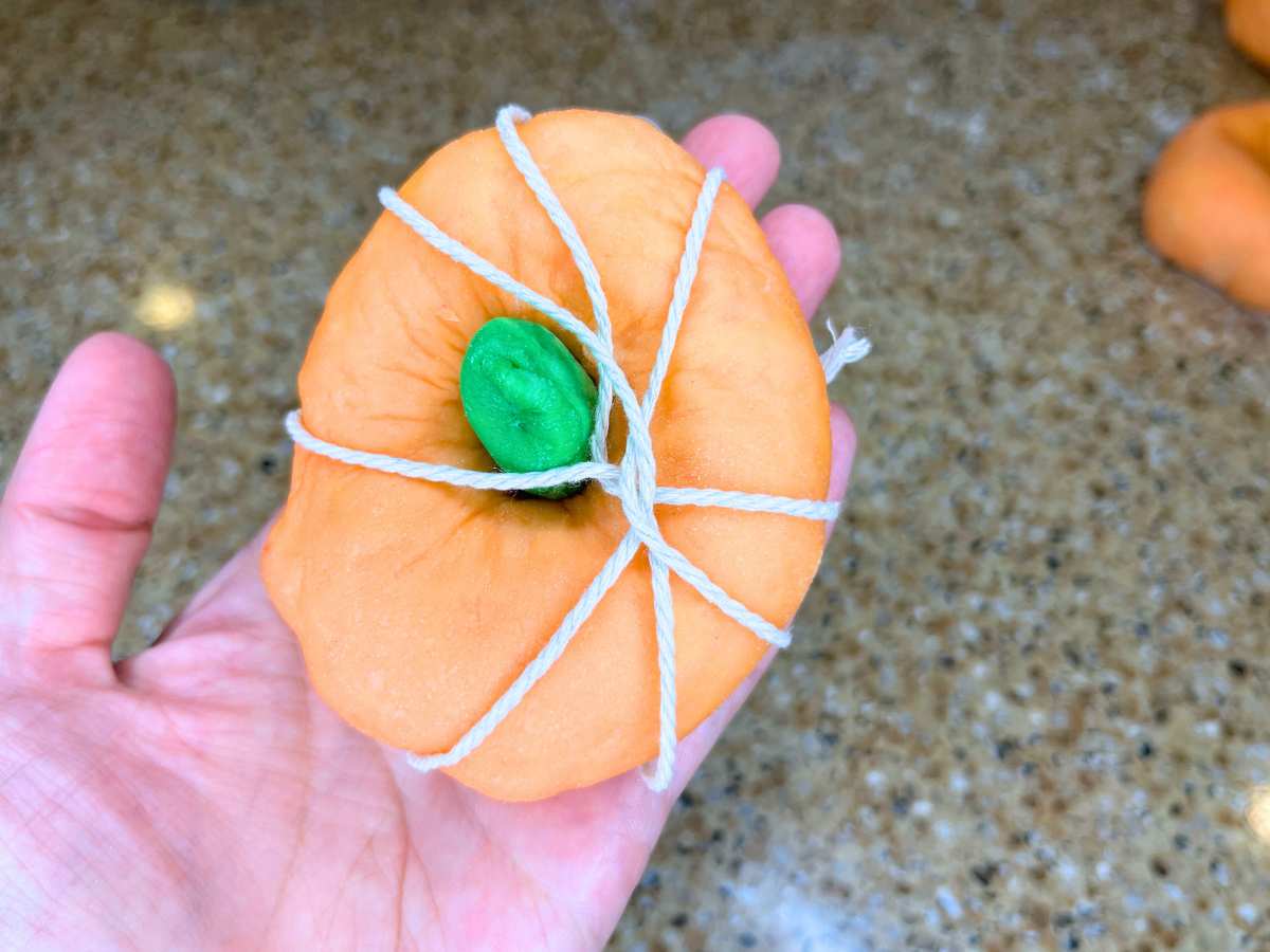 A woman holding orange and green dough wrapped in kitchen twine.