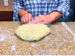 A woman is wrapping pie dough in plastic wrap.