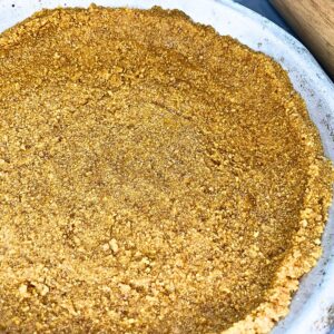 There is a metal pie plate with a graham cracker crust inside.