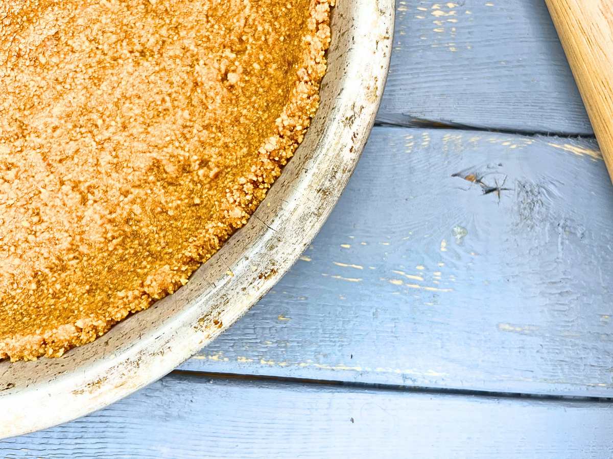 There is a graham cracker pie crust on a blue wooden table.