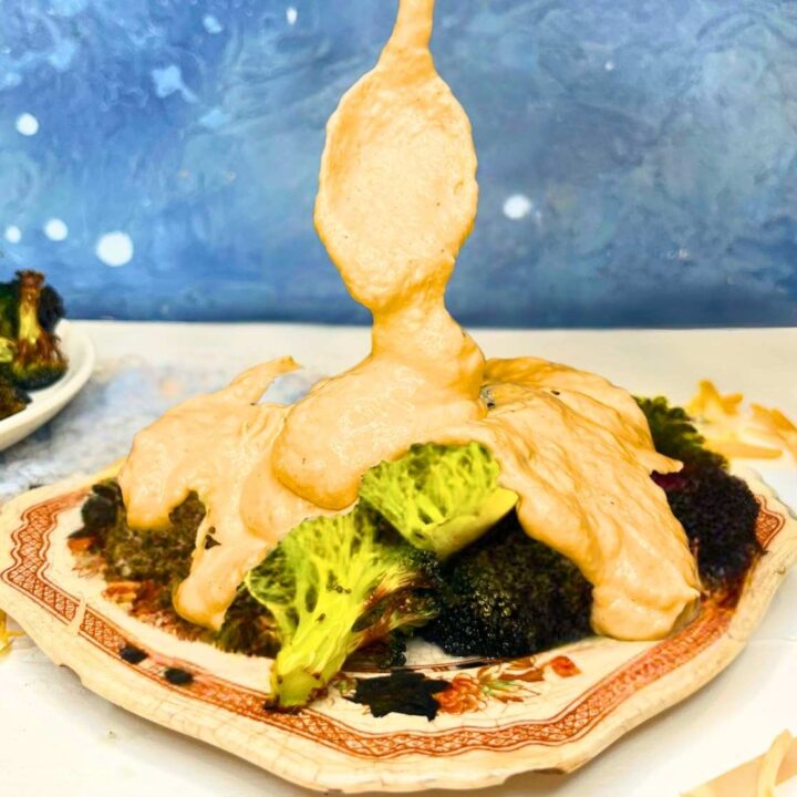 A woman is spooning cheese sauce onto a plate of broccoli.