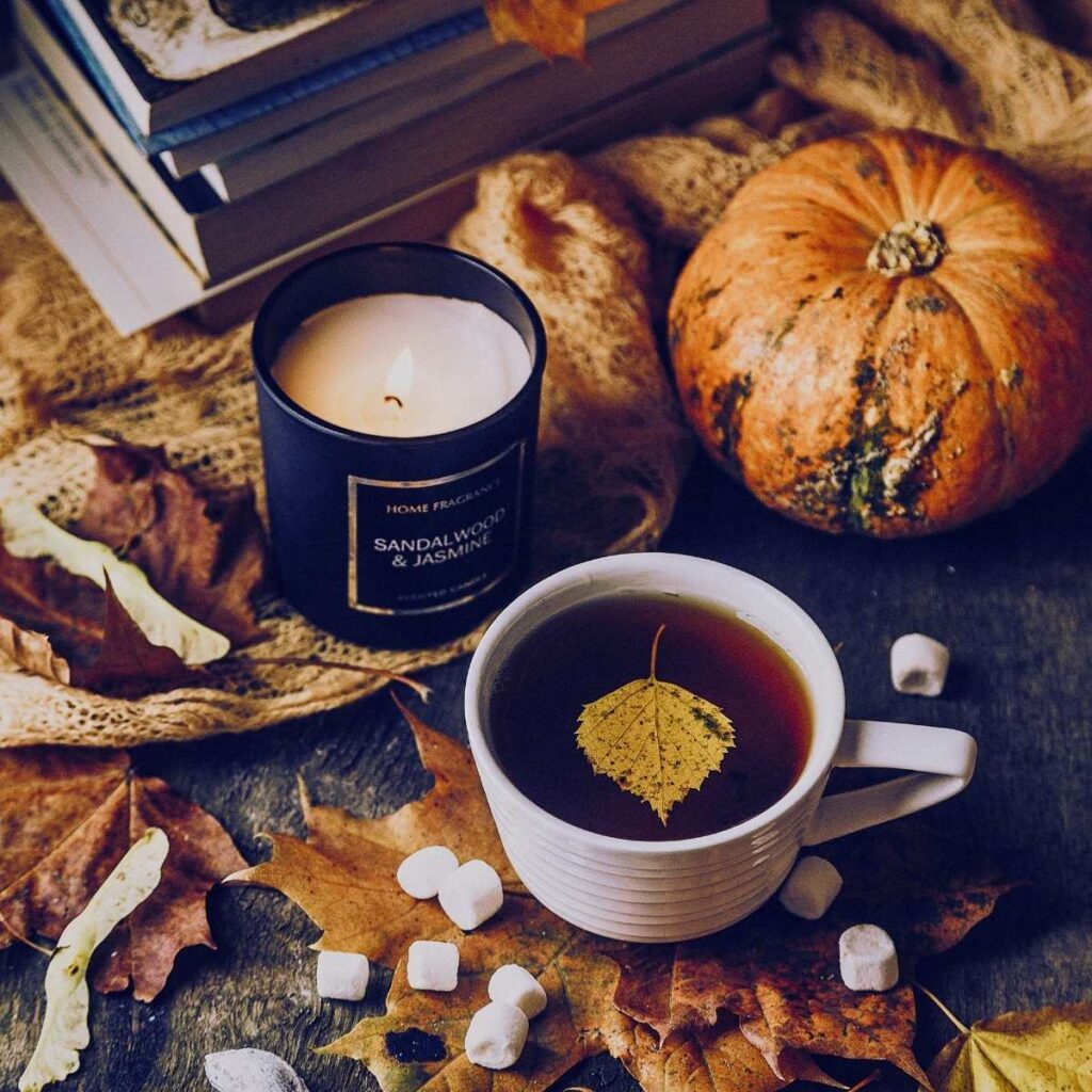 A cup of tea with a leaf in it. Behind is a candle and some gourds. 