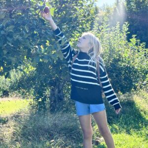 A young girl is picking apples from a tree.