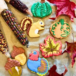 Some cookies decorated with royal icing. There are pumpkins, a squirrel, acorns, and a turkey. There are leaves and Indian corn.