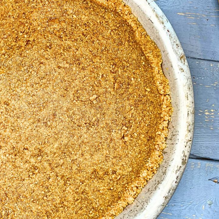 A baked graham cracker crust in a metal pie plate. There is a rolling pin beside.