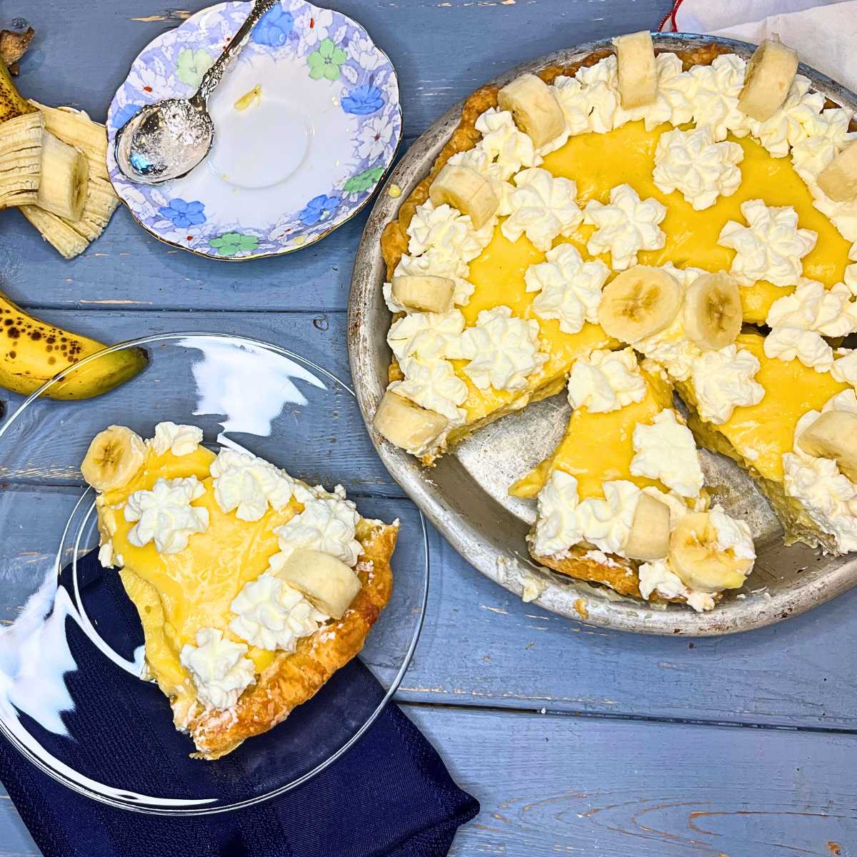 There is a sliced banana cream pie. There is a glass plate beside with a slice of pie on it.