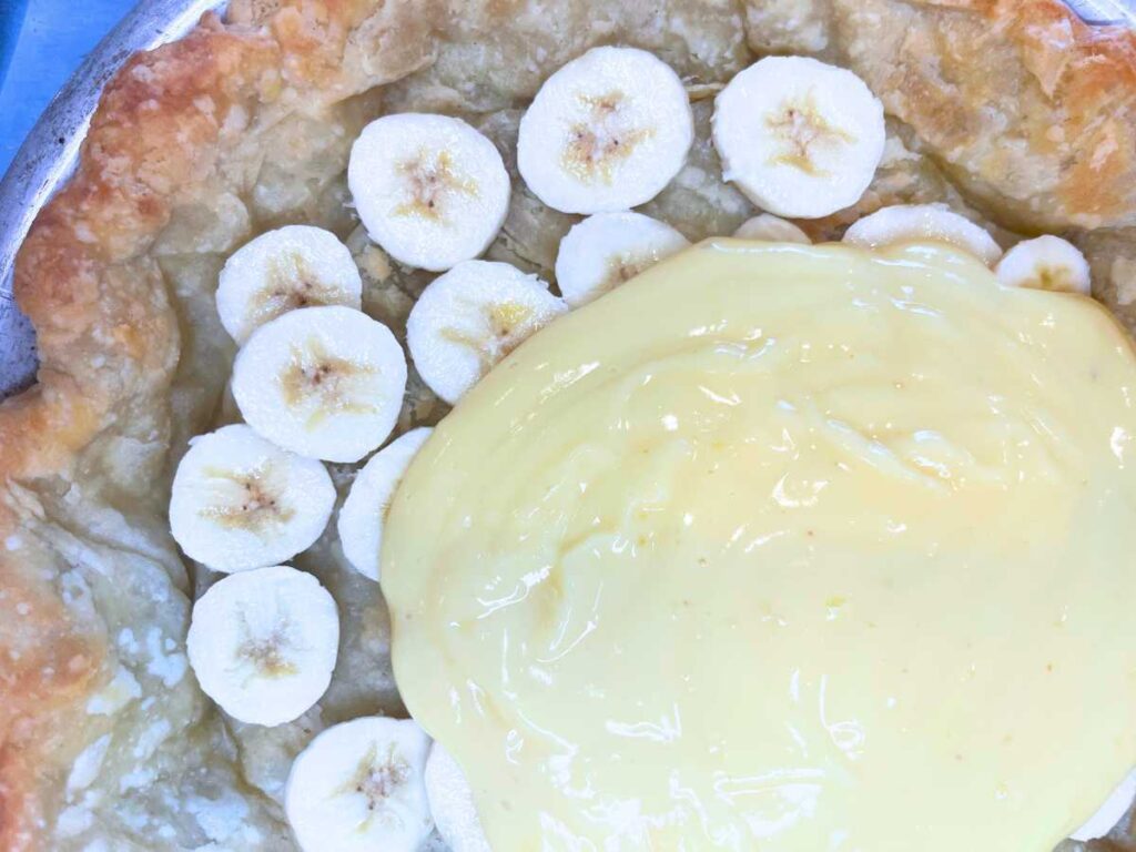 A woman is pouring banana pudding into a baked pie crust with banana slices layered on the bottom.