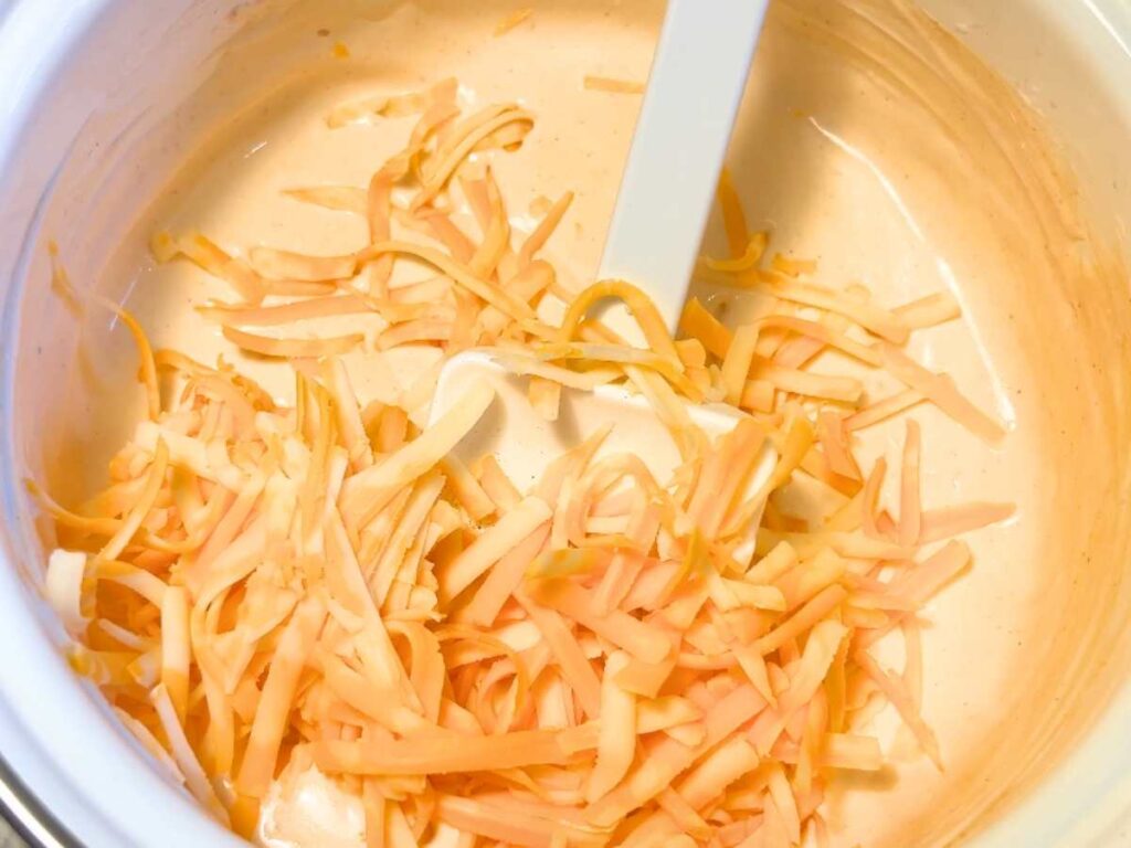 There is a sauce pot with a creamy sauce and shredded cheese on top.