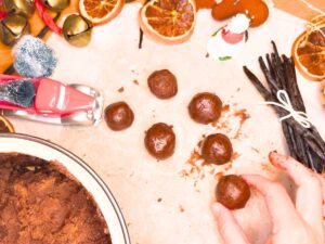 A woman is placing a rolled chocolate truffle onto a piece of parchment paper.