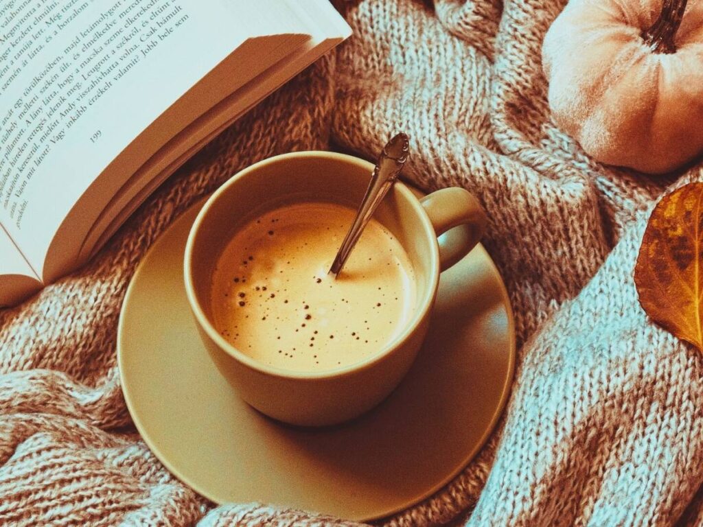 There is a mug with cappuccino and a book off to the side.