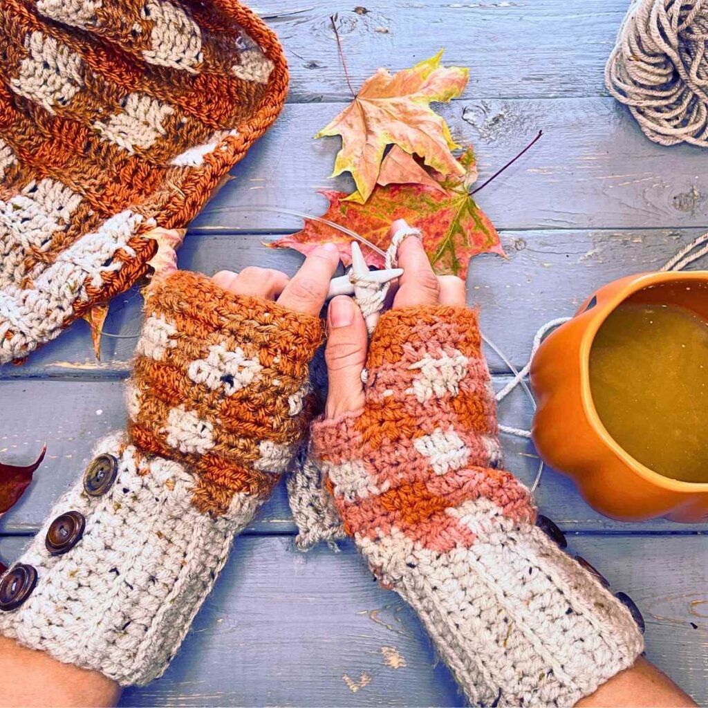 A woman is wearing orange and grey crochet gloves. She is knitting.