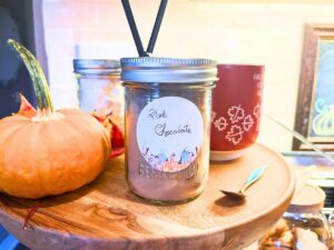 A wooden two tiered shelf with fall mugs, hot chocolate, and marshmallows.