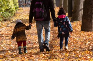 A dad and two children are walking in fall leaves.