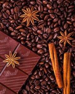 There are coffee beans with a bar of chocolate, star anise, and cinnamon on top.