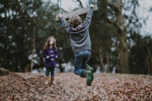 Two children are playing out doors. There are fall leaves around.