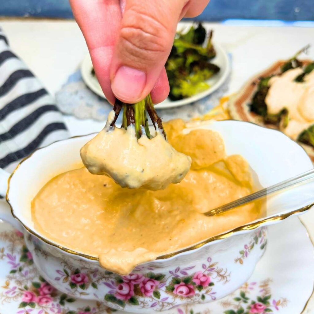 A woman is dipping broccoli into a dish of cheese sauce.