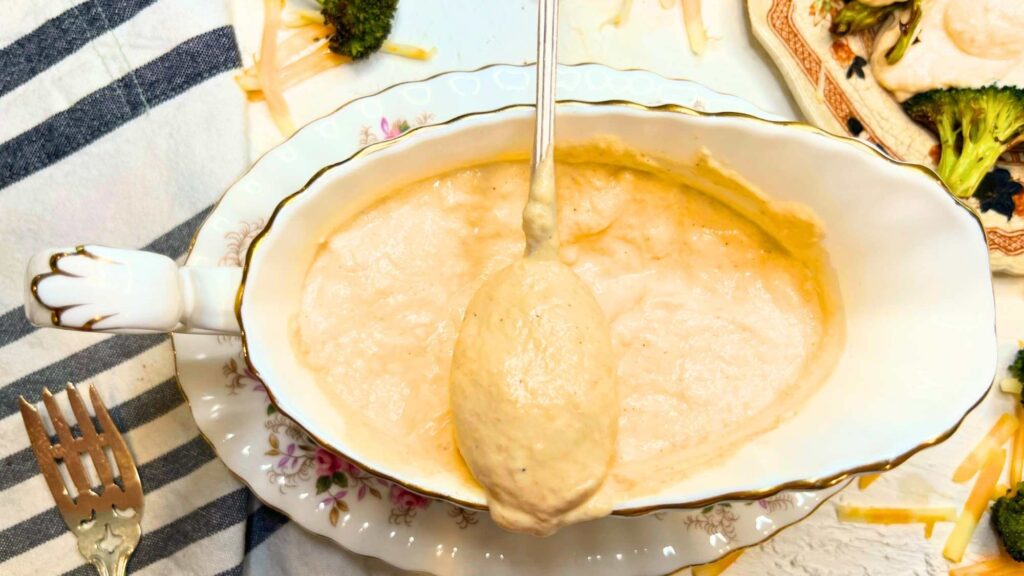 A spoon full of cheese sauce is resting on a dish containing more sauce.