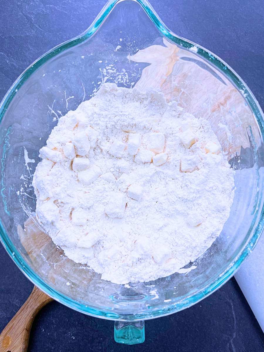 A large glass bowl with dry ingredients and butter cubes inside.