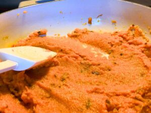 There is a woman stirring pumpkin purée in a sauce pot.