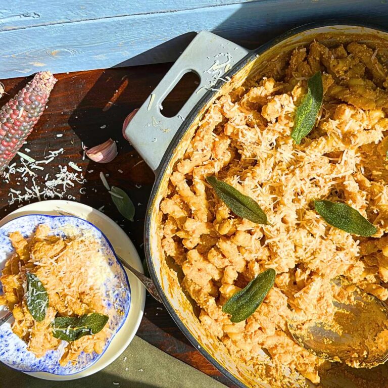 There is a pumpkin and sage pasta with sage leaves on top. There is a plate beside with a serving of the pasta.