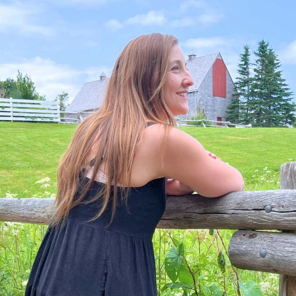 Rebecca from Flour and Filigree leaning on a wooden fence. There is a barn in the background.