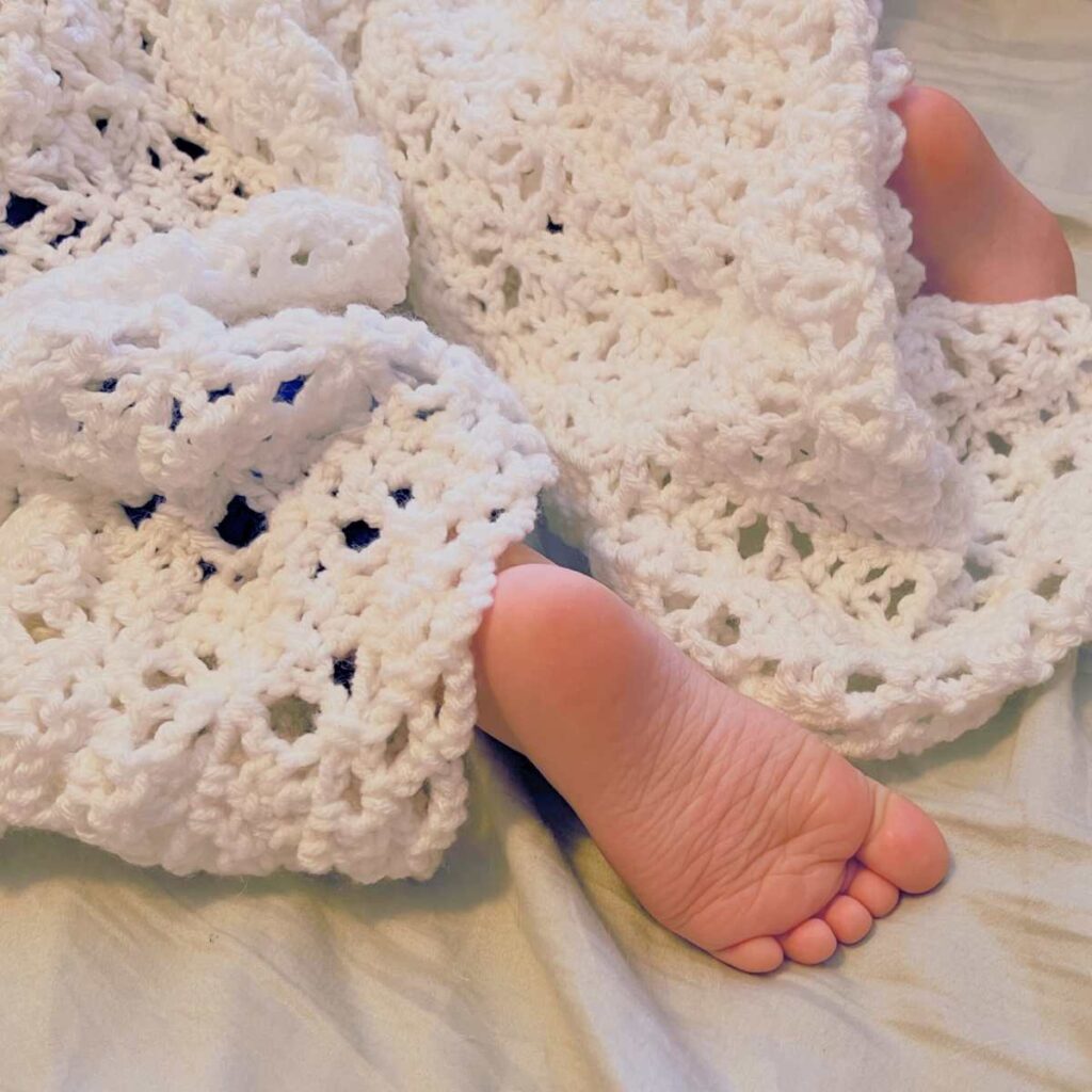 There is a small covered by a white crochet blanket.