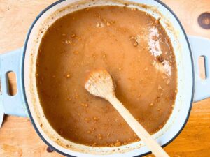 An apple butter purée inside of a large grey pot. There is a wooden spoon inside.