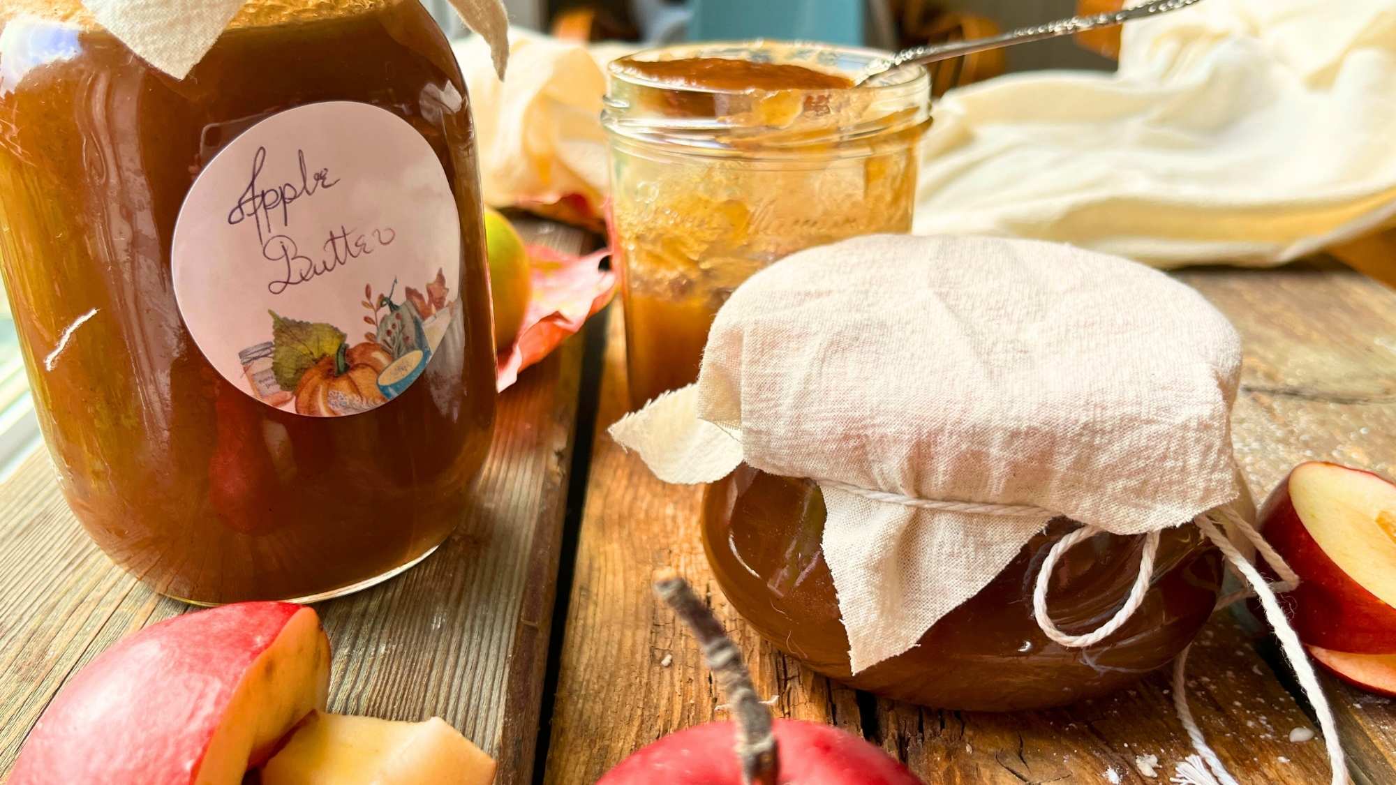 Jars of apple butter on a wooden table. There are apples around.