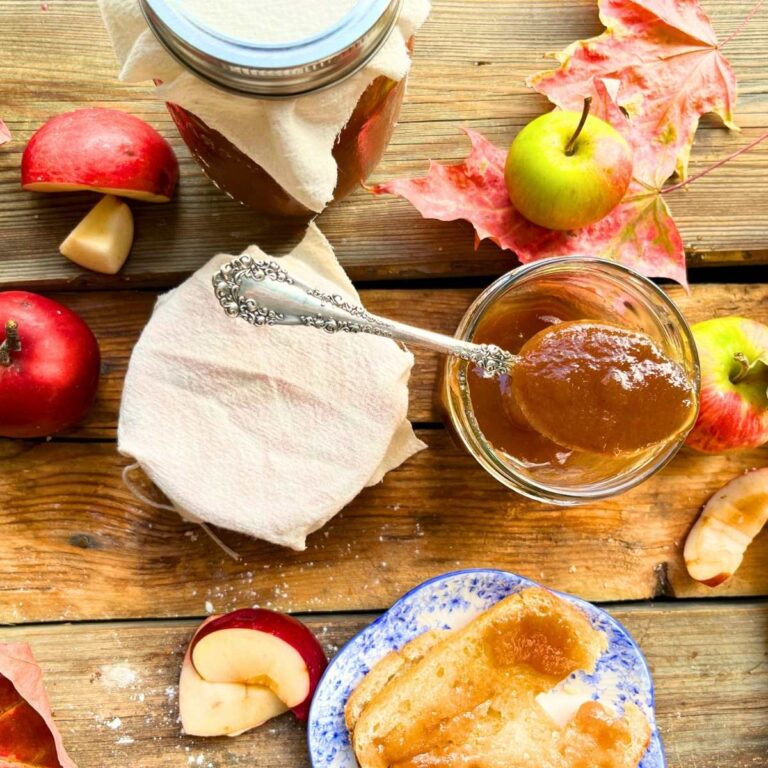 There are jars of apple butter on a wooden table. One has a spoon resting on top.