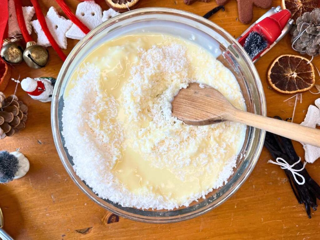 A large glass mixing bowl full of coconut and sweetened condensed milk.