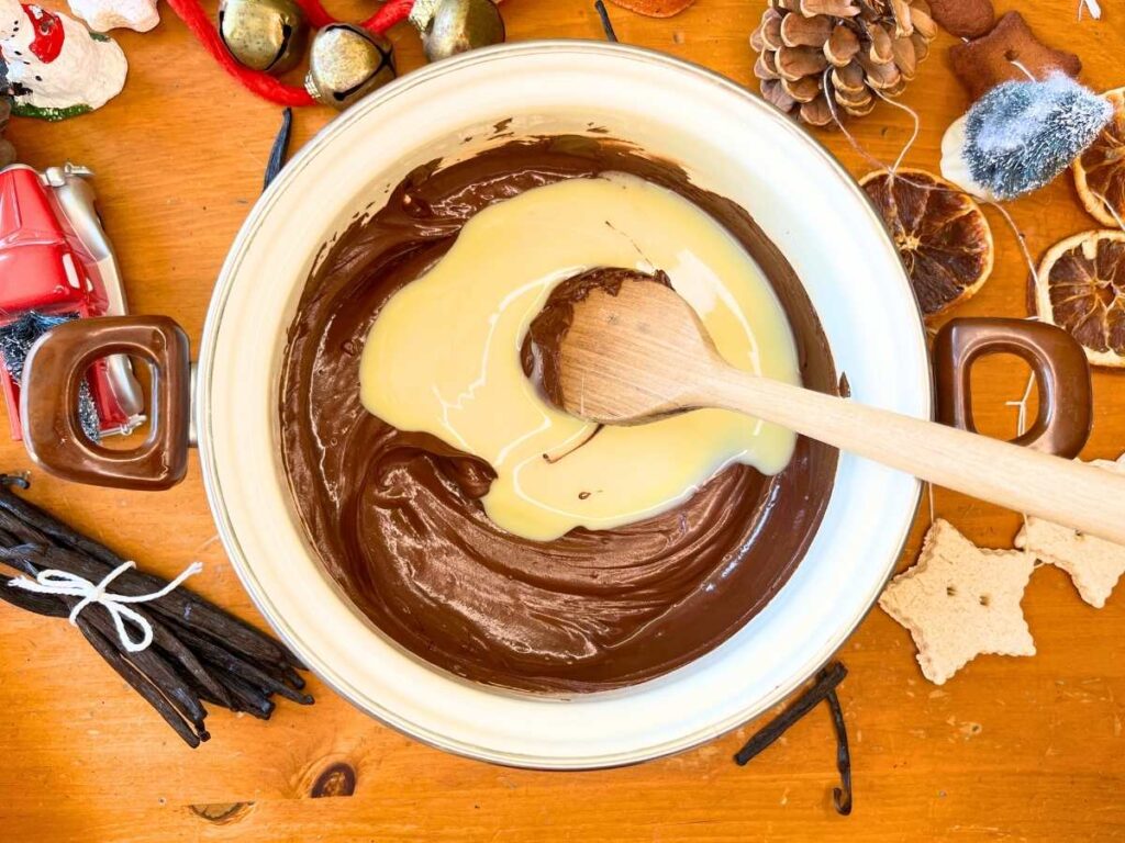 A pot of melted chocolate with sweetened condensed milk inside. There is a wooden spoon inside the pot.