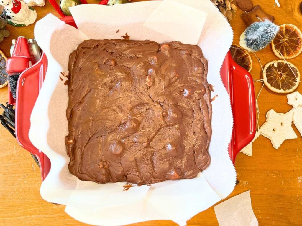 A red casserole dish lined with parchment paper. There is a chocolate mixture spread inside.