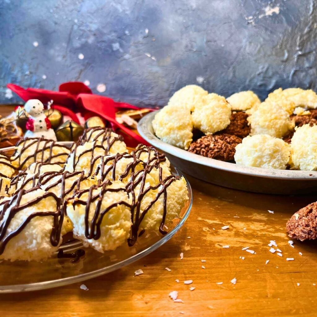 Coconut macaroons on a glass plate with chocolate drizzle on top. There are more in the background in a metal pie plate.